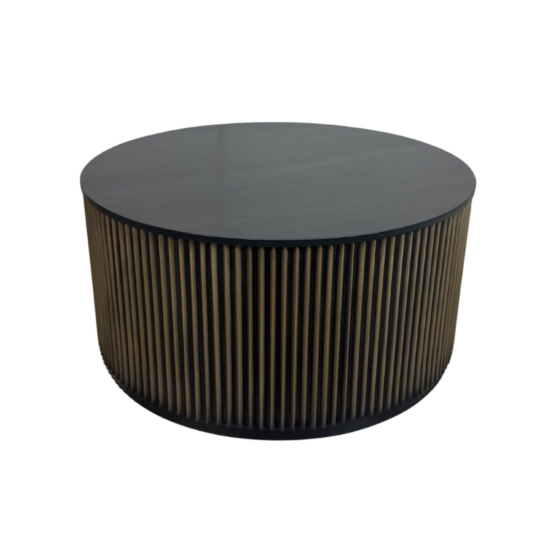 Round drum coffee table with black top and ribbed brass-toned sides, dark base