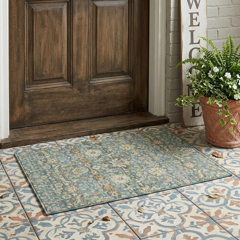 Washable indoor/outdoor area rug laid flat on tile floor with teal blue floral pattern