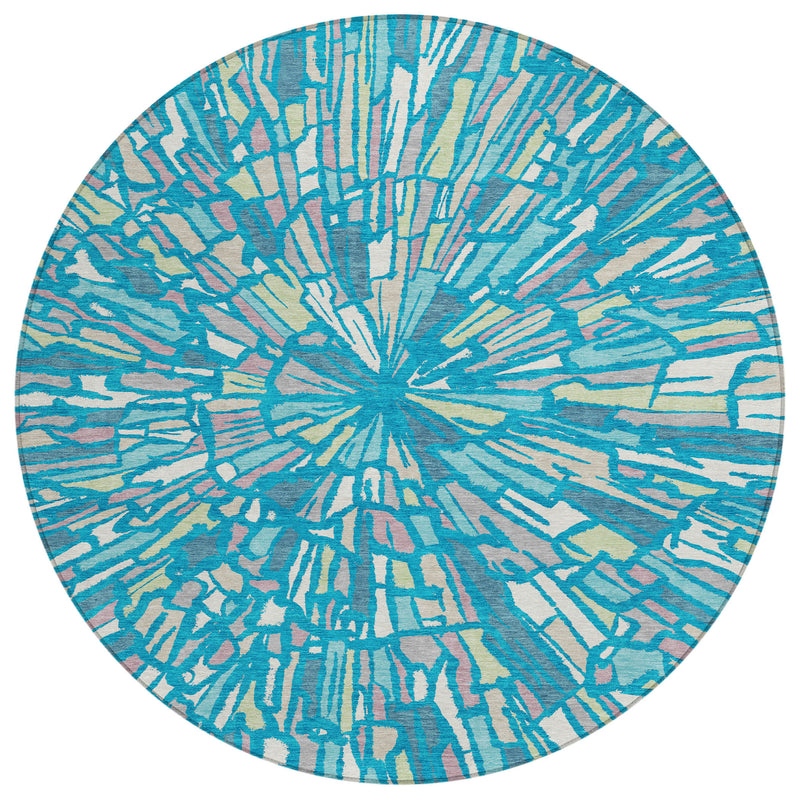 Round abstract area rug featuring teal-blue sunburst design with cream and green streaks.