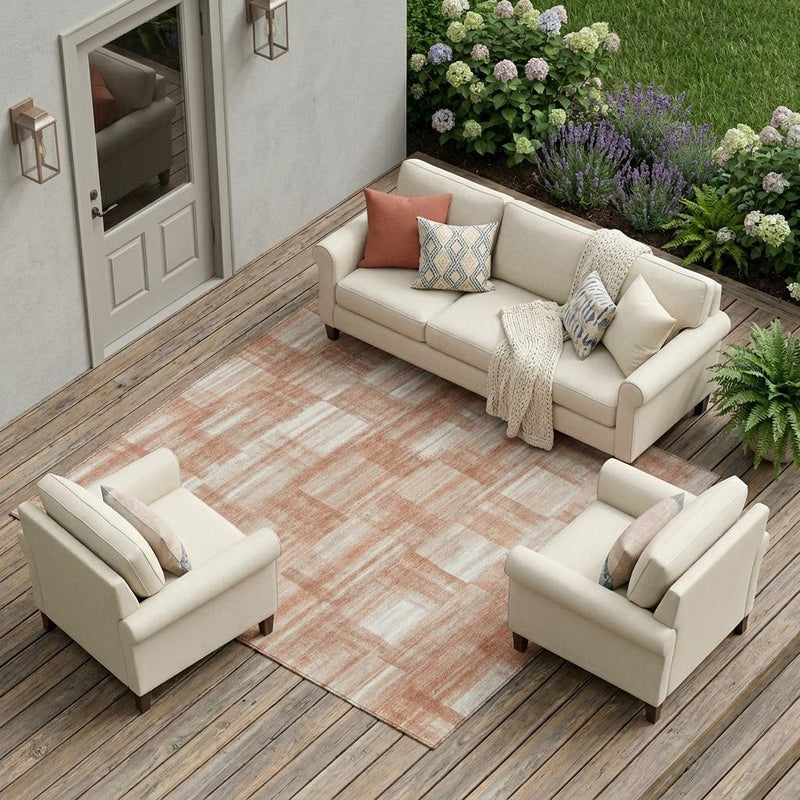 Cream upholstered outdoor sofa set with coral accents, featuring a geometric rug, set in a lush garden.