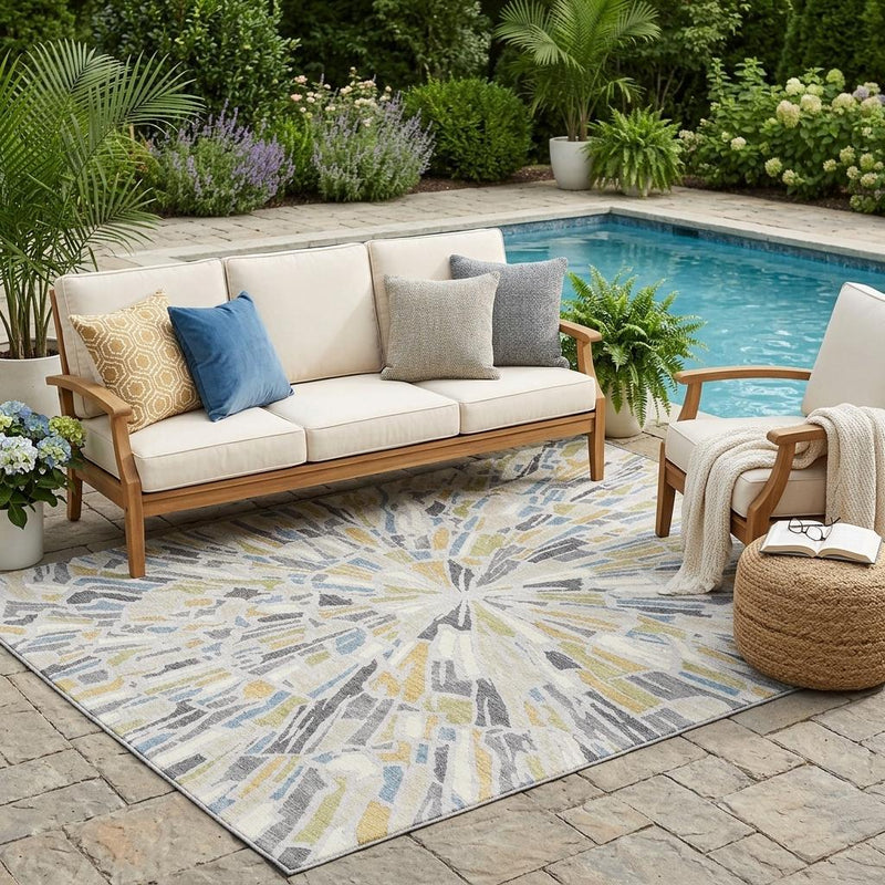 Outdoor patio area rug with abstract sunburst design in gray, blue, and yellow accents.