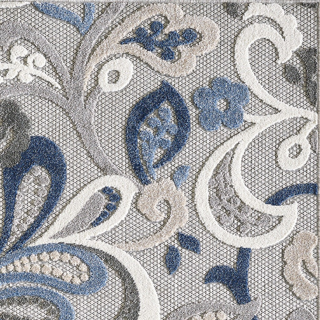 Close-up indoor/outdoor area rug: blue-and-gray ornamental floral pattern on light background