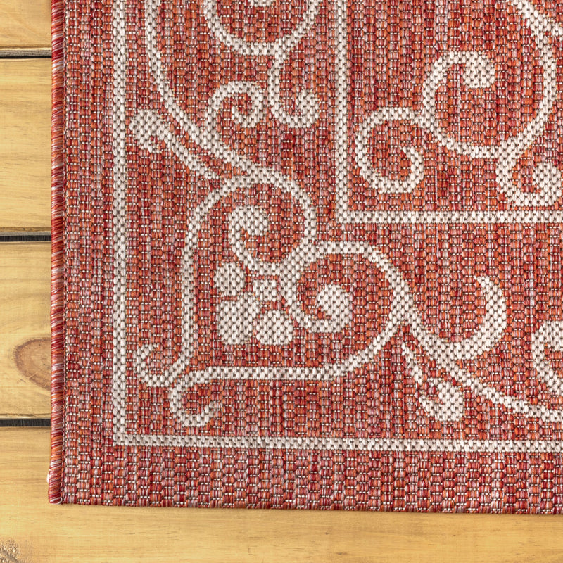 Indoor/outdoor area rug with red field and light beige medallion and scrollwork border