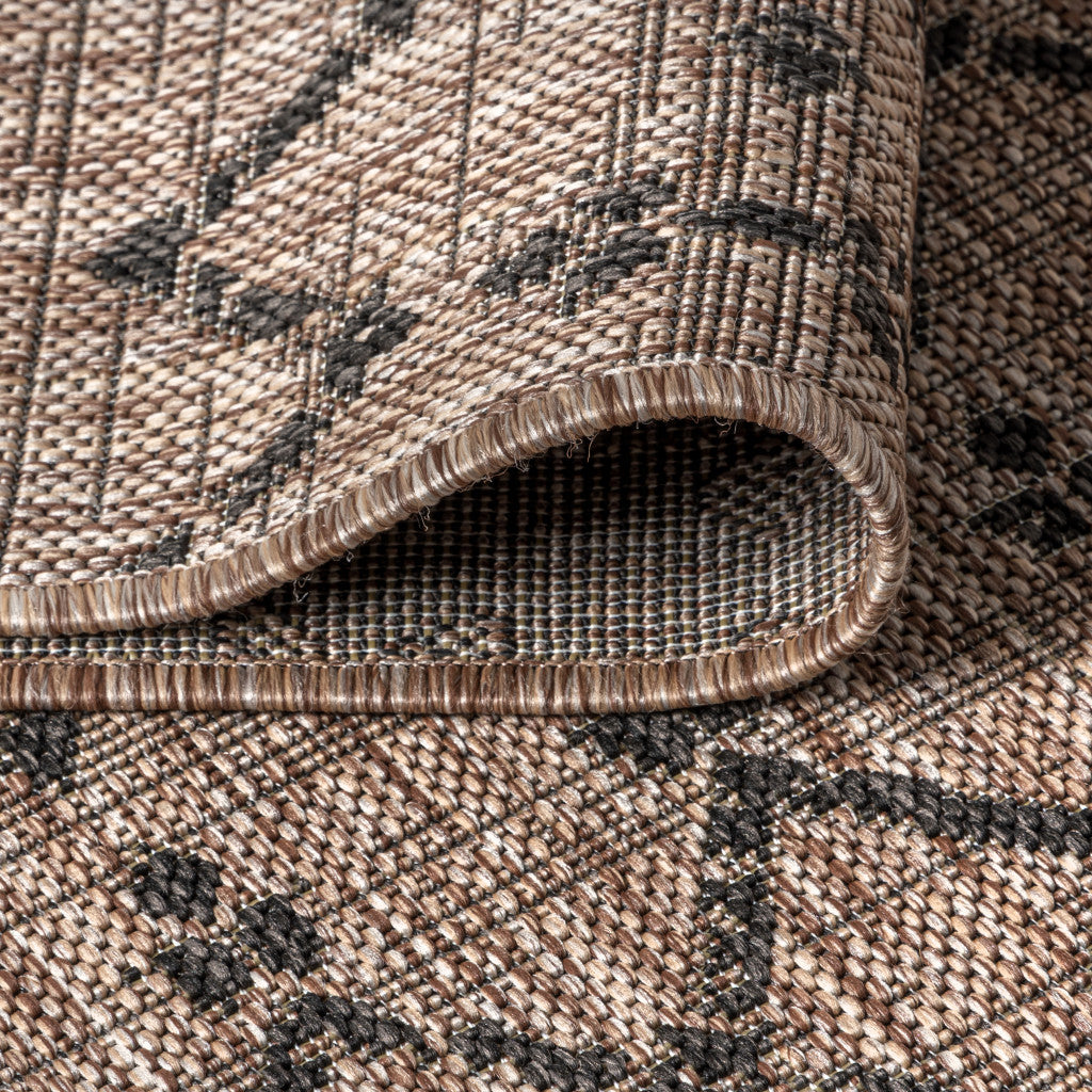 Close-up of round beige rug pile with black trellis pattern and stitched edge binding.