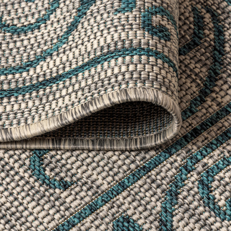 Woven area rug close-up showing gray loops, teal accents, and flat braided edge.