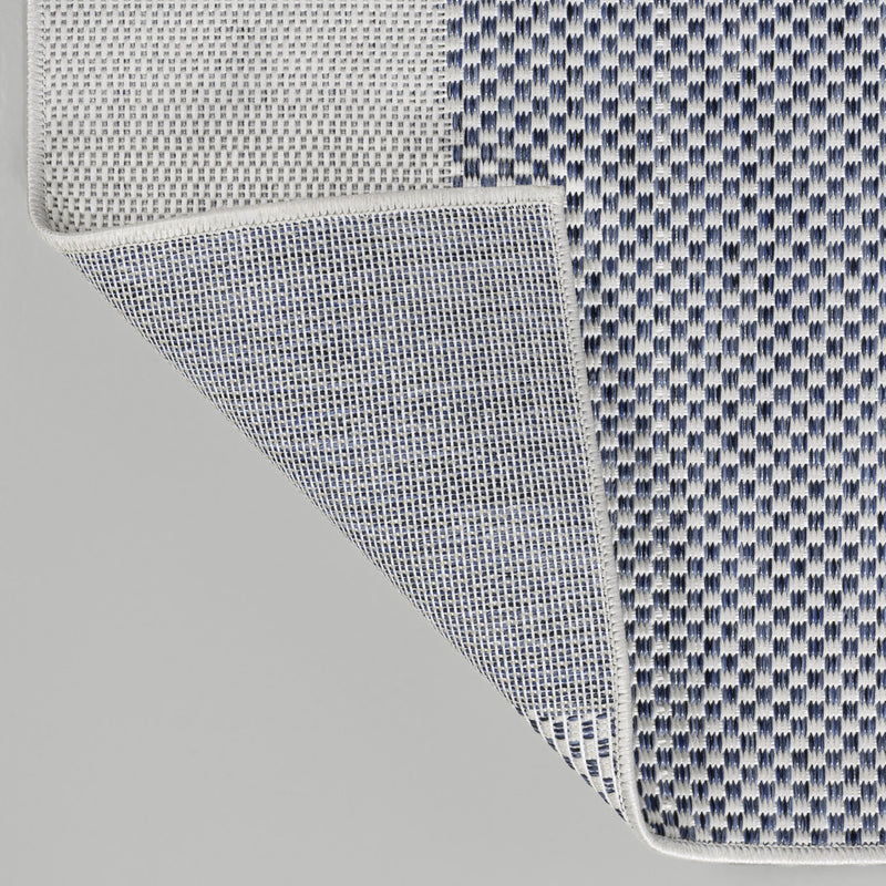 Cream and navy geometric area rug corner showing stitched edge and layered backing