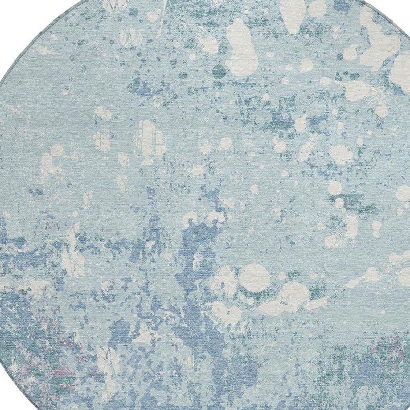 Close-up of round light blue area rug with beige abstract splatter and speckles.