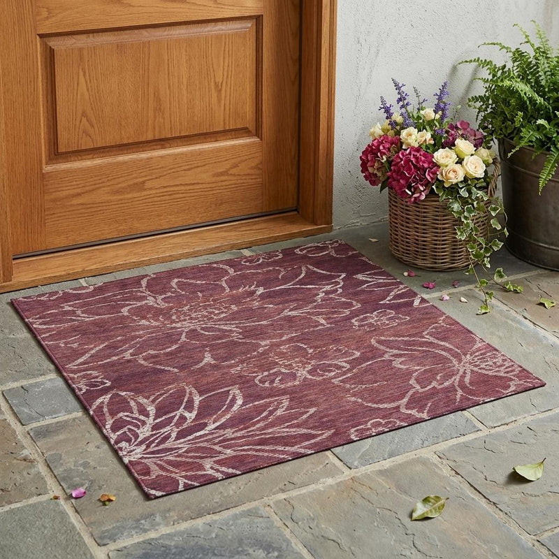 Indoor outdoor area rug in eggplant with cream floral pattern, laid on stone patio