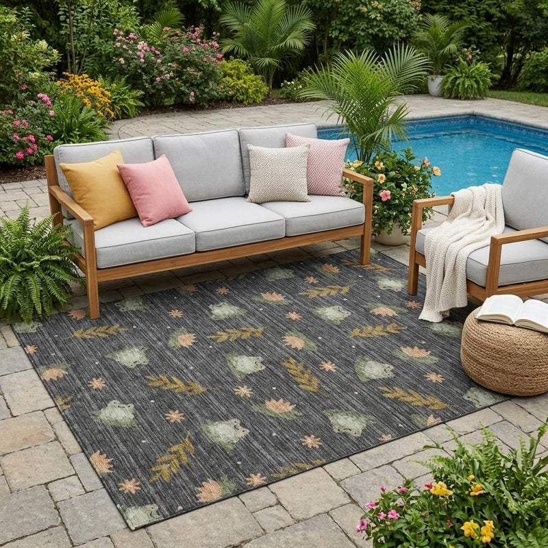 Indoor-outdoor area rug on patio, dark charcoal with leaf-and-bunny botanical pattern.