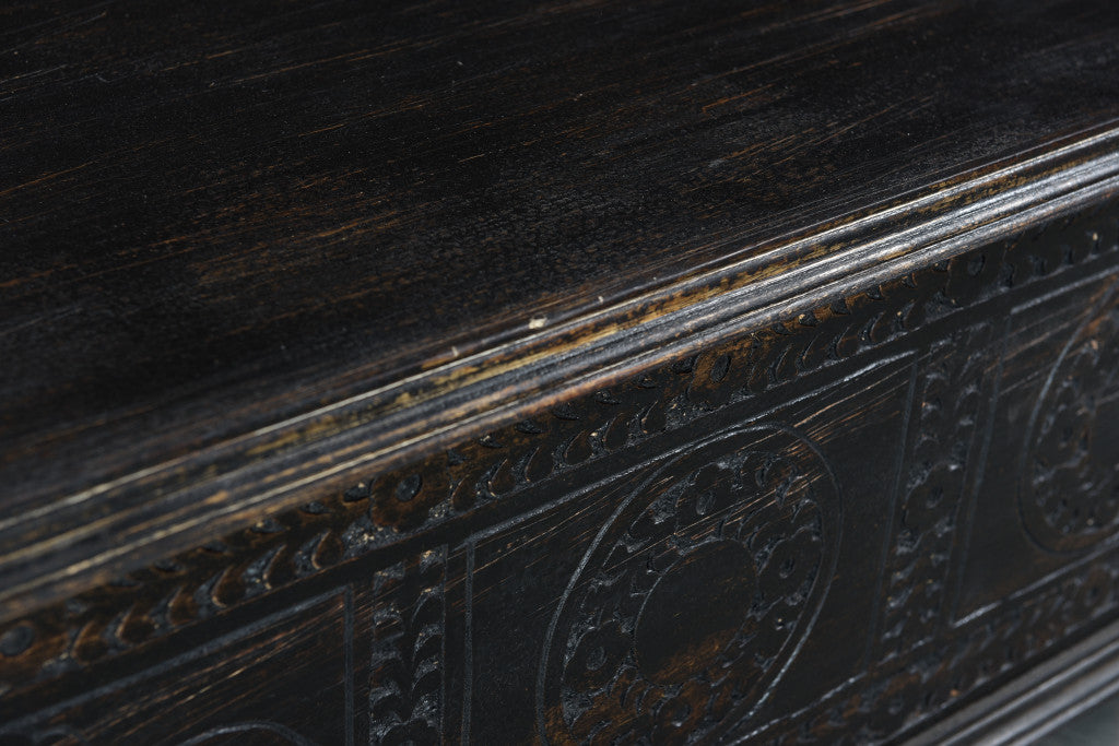 Close-up of black distressed coffee table top edge with carved border detailing.