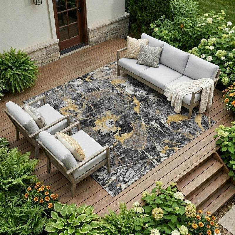 Abstract indoor outdoor area rug on deck boards with charcoal and gold floral pattern
