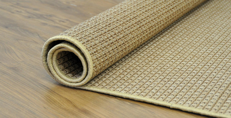 Rolled beige flat-woven area rug on wood floor, stitched edge visible