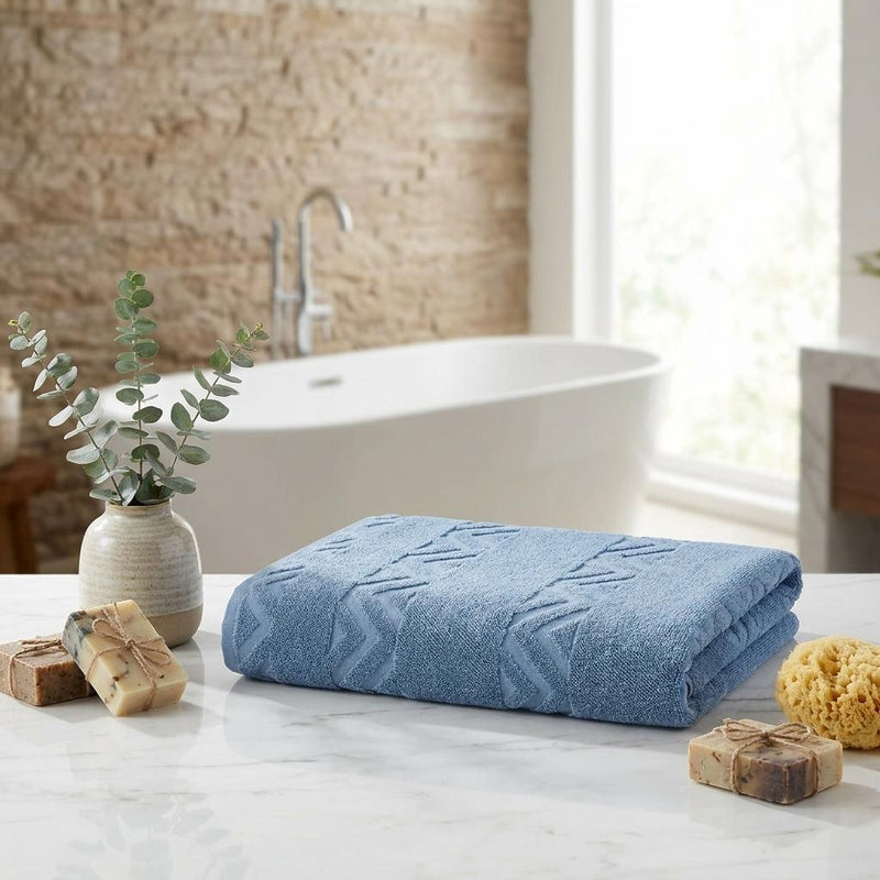 Blue jacquard bath sheet towel folded on a countertop, featuring chevron pattern