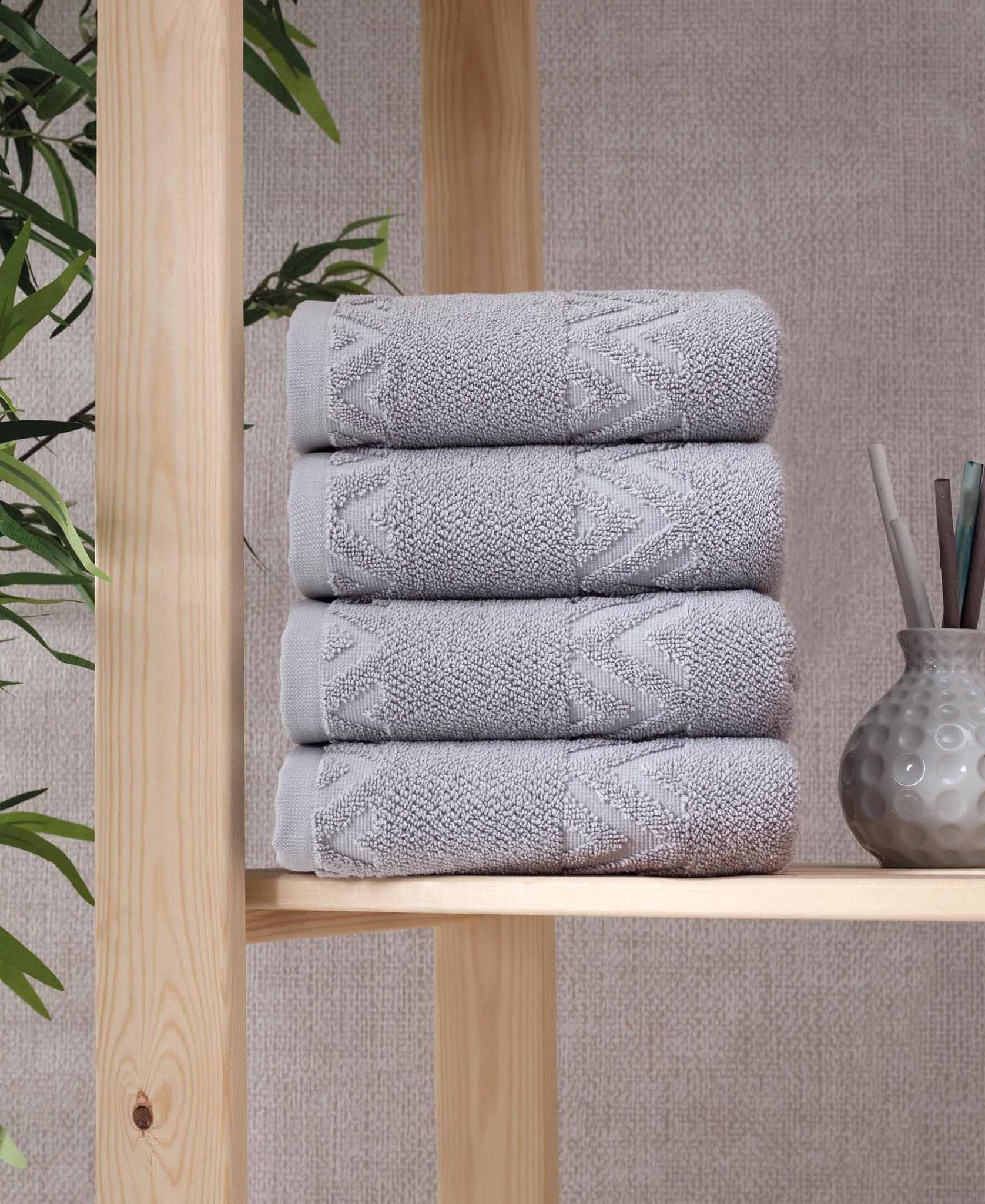 Set of four light gray hand towels folded on a wooden shelf, geometric zigzag pattern.