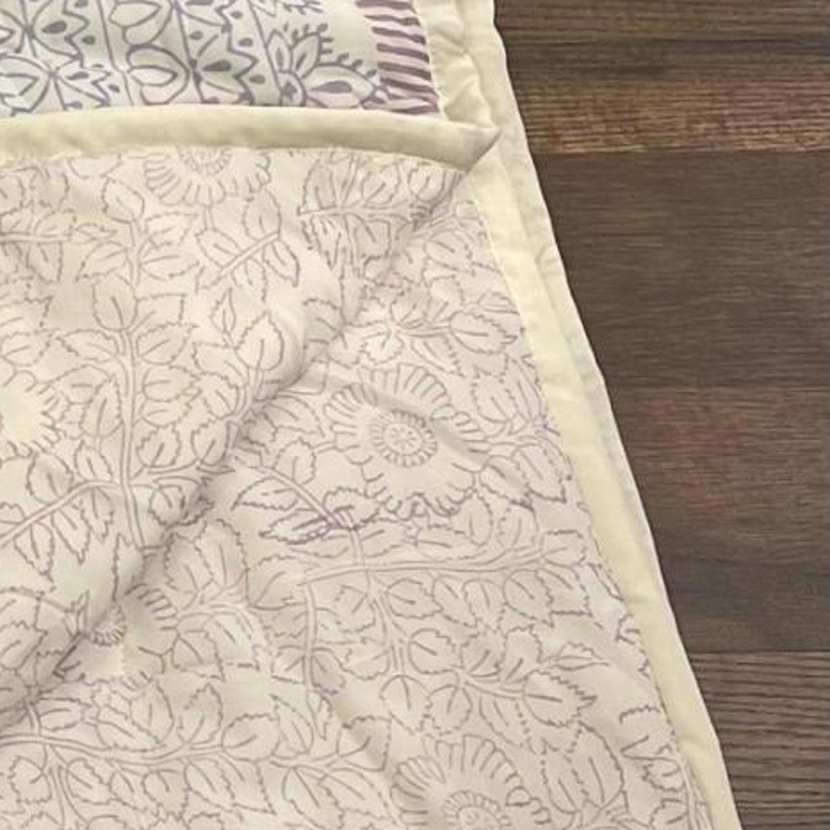 Floral cotton comforter with cream base and sage-lavender botanical pattern, stitched edge
