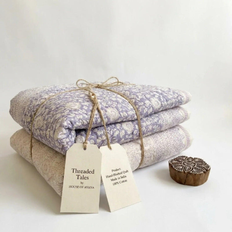 Folded floral cotton comforters in cream and sage-lavender, tied with twine and tags
