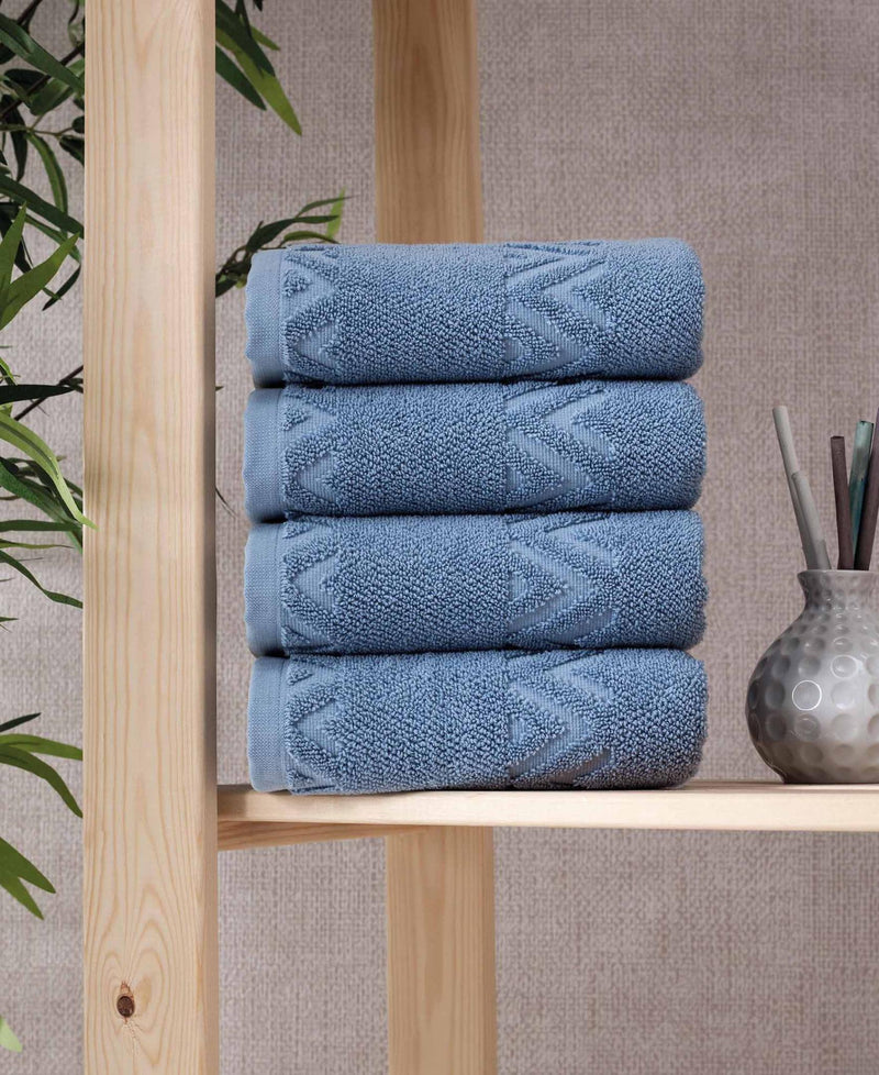 Four folded blue hand towels with geometric chevron motif, displayed on wooden shelf