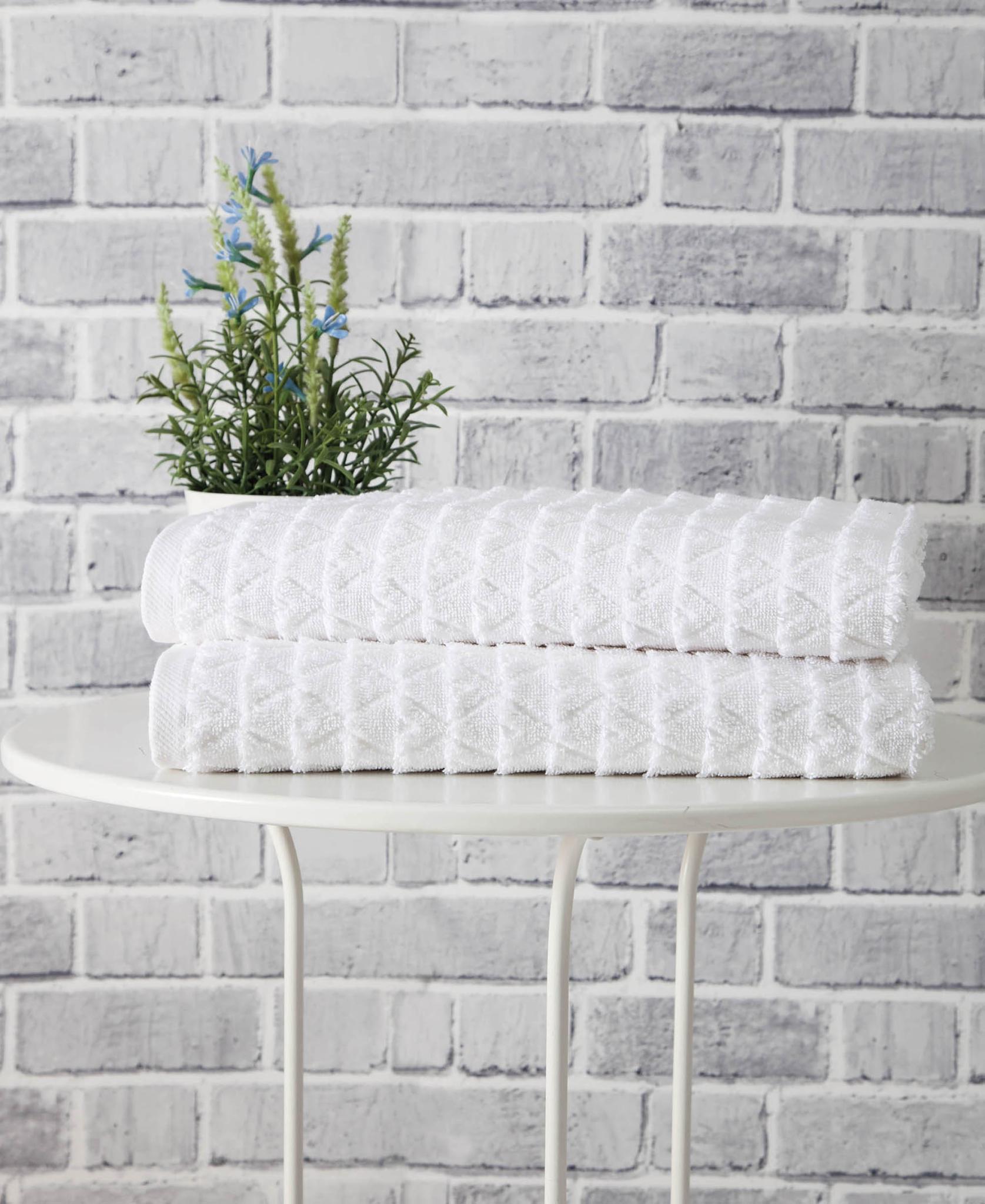 Set of two white bath towels folded on a small stand, textured geometric weave