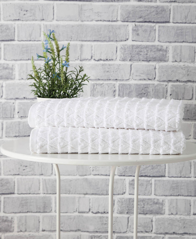 Set of two white bath towels folded on a small stand, textured geometric weave
