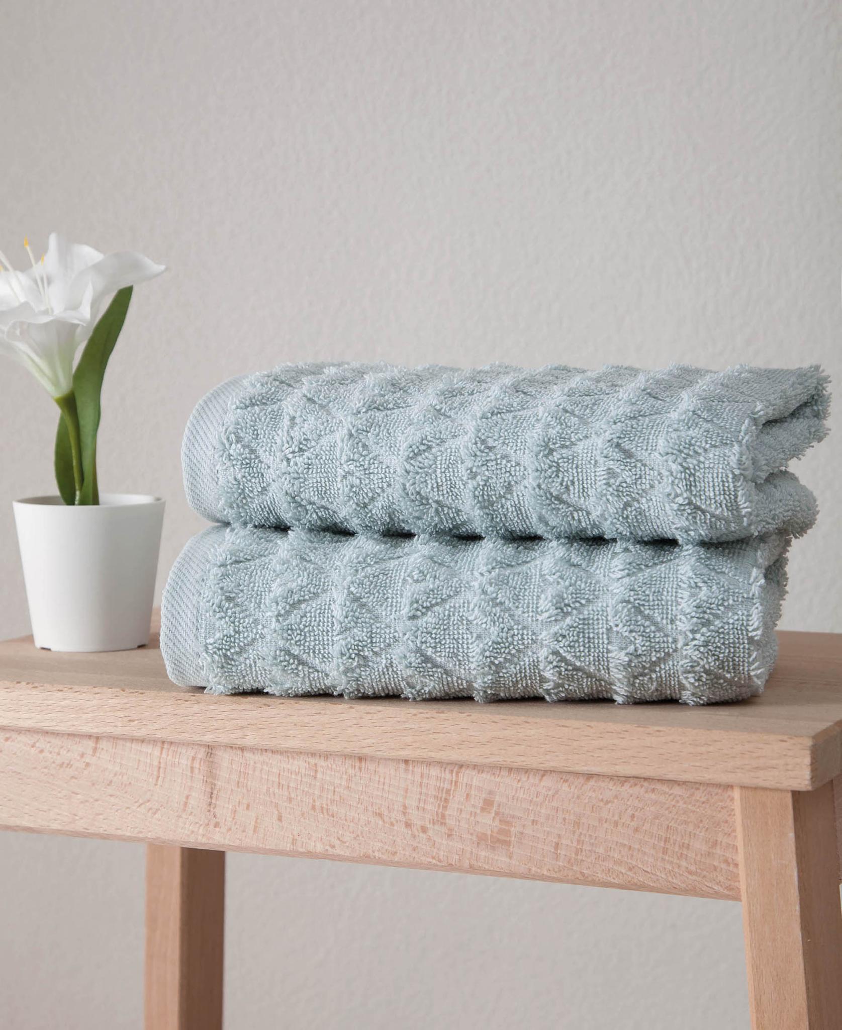 Folded aqua Turkish hand towels on wooden surface, textured geometric pattern.