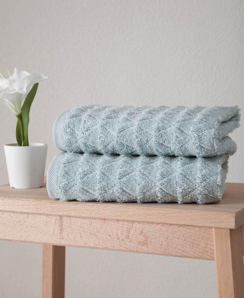 Folded aqua Turkish hand towels on wooden surface, textured geometric pattern.