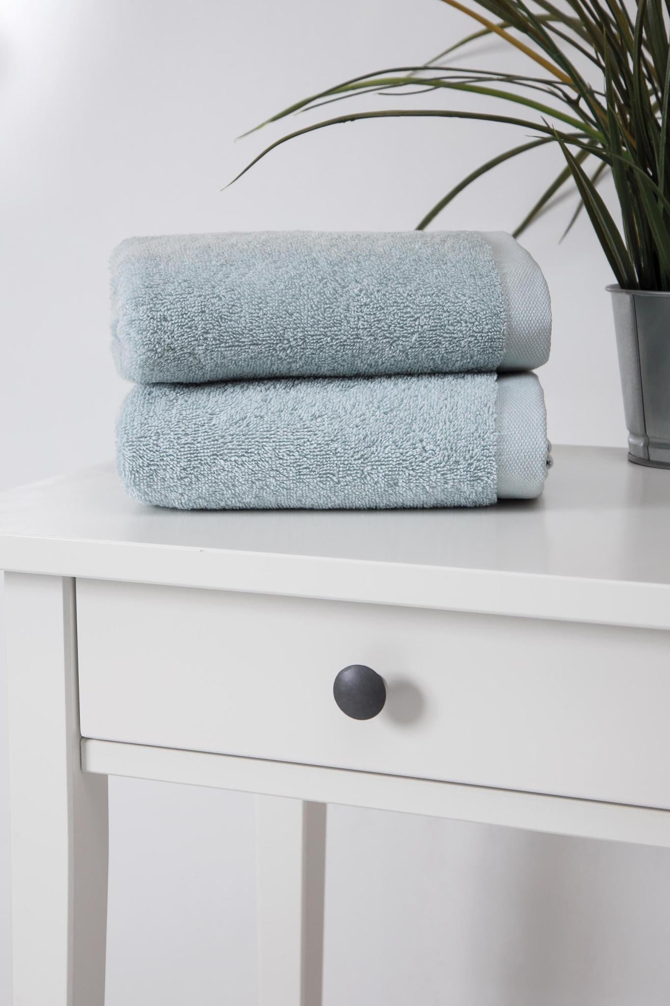 Set of two light blue Turkish cotton hand towels, folded and stacked on a shelf.