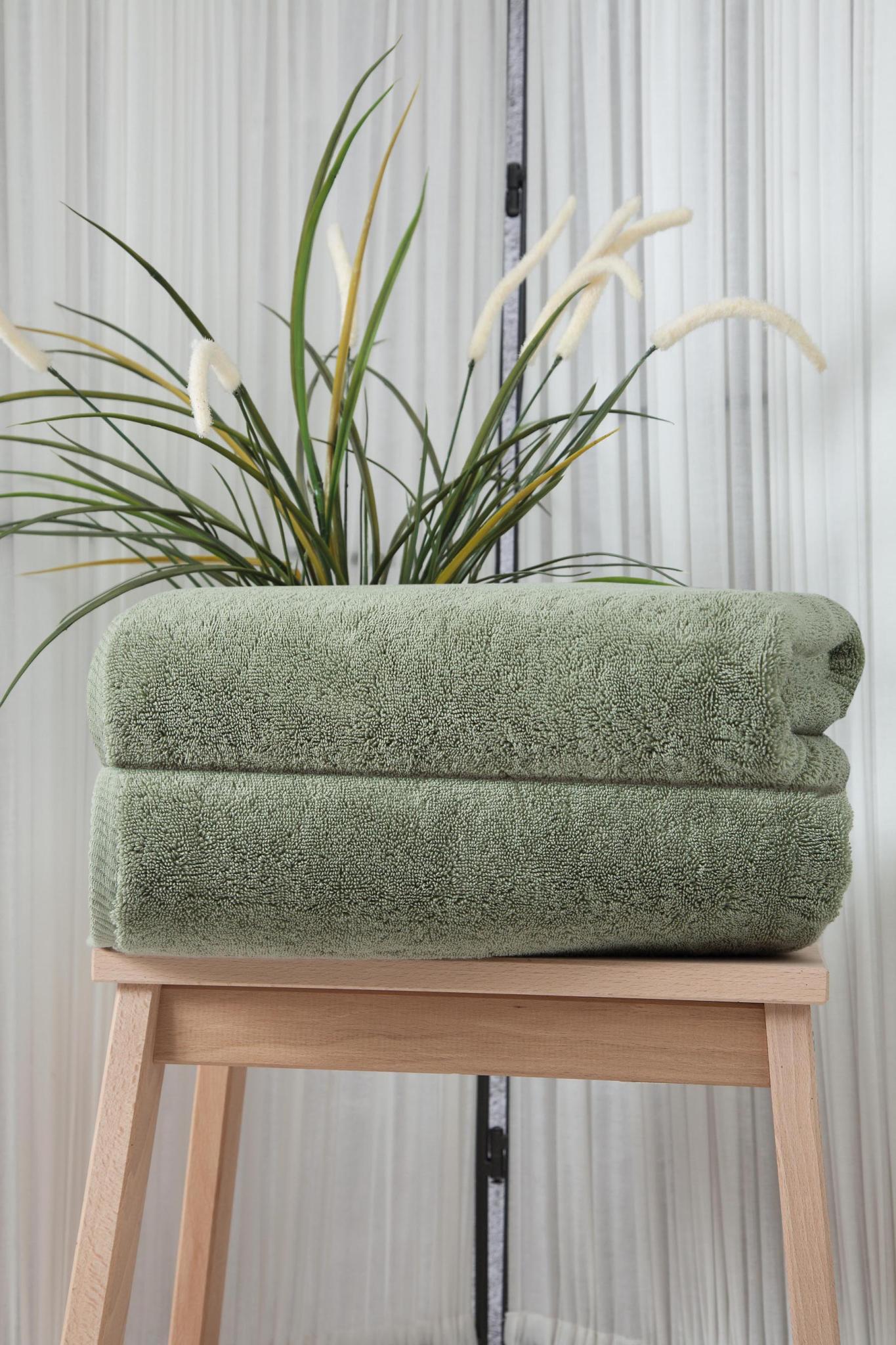 Set of two green Turkish cotton bath towels, folded on wooden stool