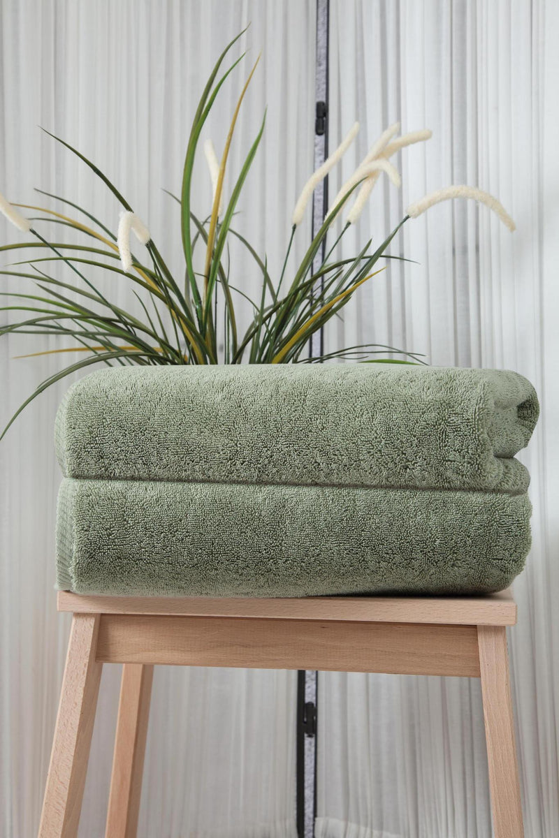 Set of two green Turkish cotton bath towels, folded on wooden stool