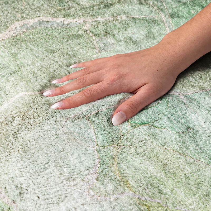 Hand pressing down on green and teal abstract shag area rug to show soft, dense pile.