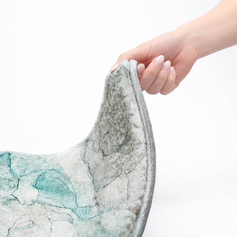 Shag area rug corner lifted by hand, teal-gray abstract pattern with gray binding