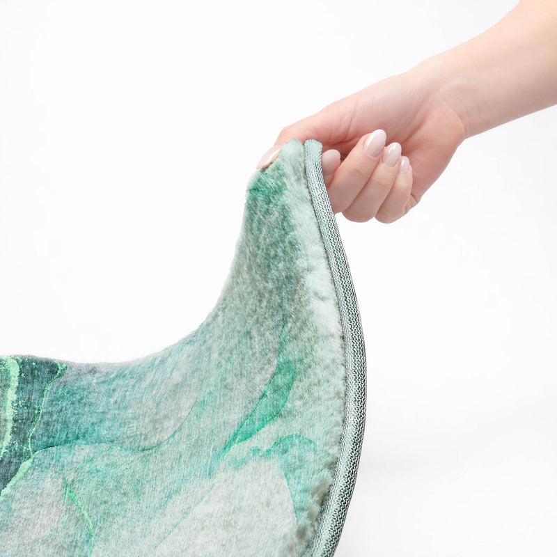 Washable shag area rug with green and teal pile and gray binding, edge lifted