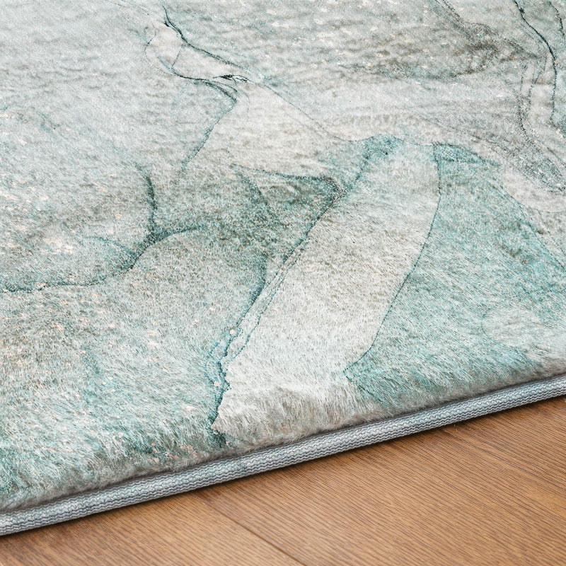 Close-up of teal and gray abstract shag area rug with gray bound edge