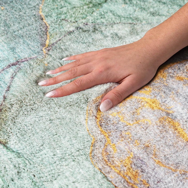 Hand pressing a shag round rug, showing soft pile over teal and gray abstract pattern.