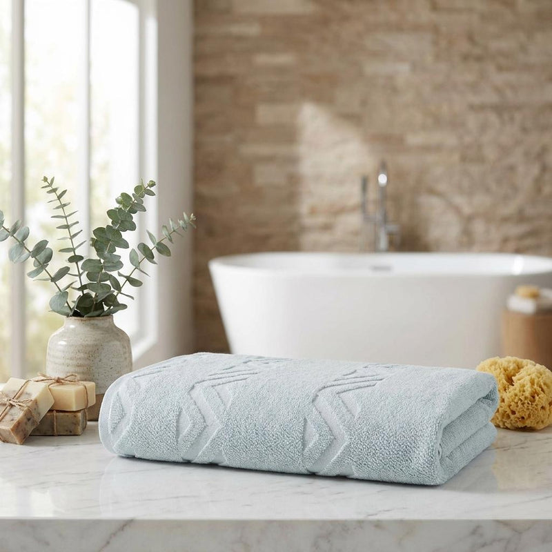 Aqua bath towel rolled on a countertop with white zigzag geometric pattern