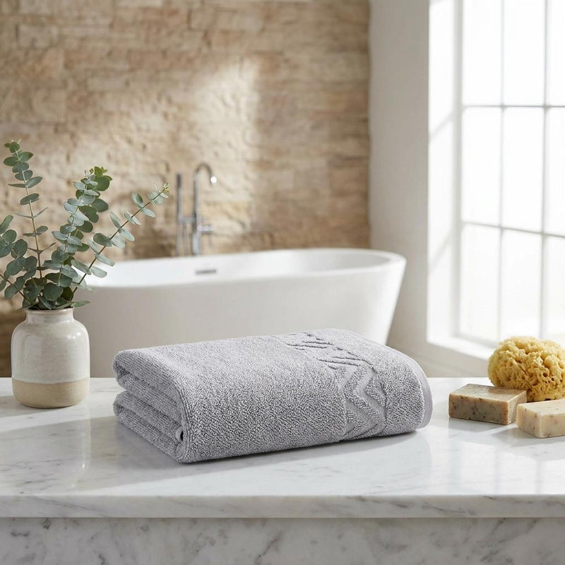 Light gray Turkish cotton hand towel folded on a bathroom countertop with geometric pattern.