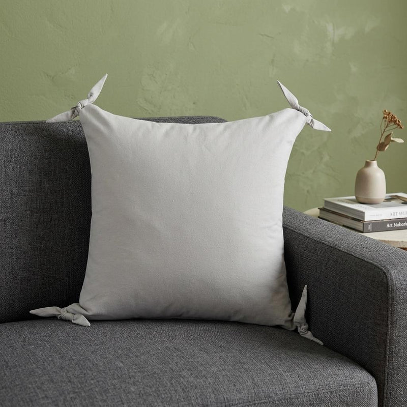 Light gray zippered cotton pillow cover with corner ties on a sofa