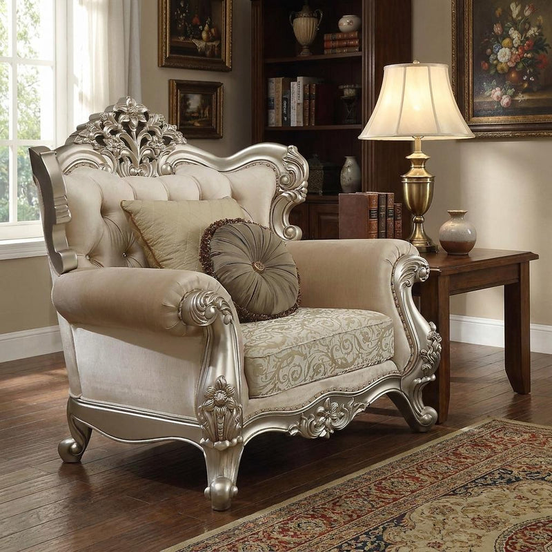 Champagne upholstered chair with damask seat panel, ornate silver legs, and decorative pillows