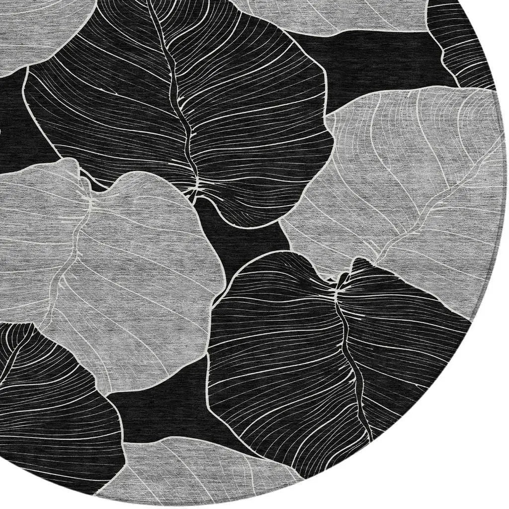 Round black and white area rug featuring abstract leaf designs in soft grey and white, perfect for modern decor.