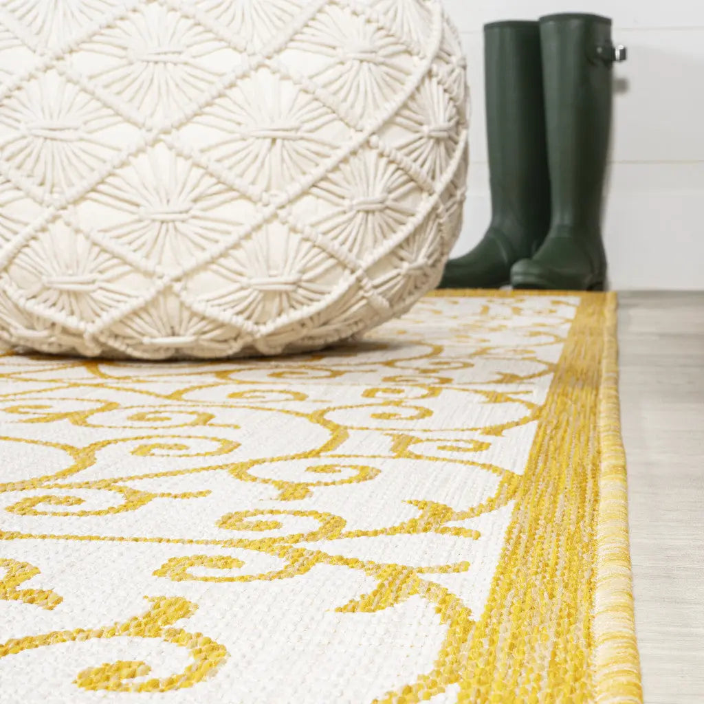 Beige patterned rug with yellow details, textured white pouf, and green rain boots, perfect for a stylish entryway.