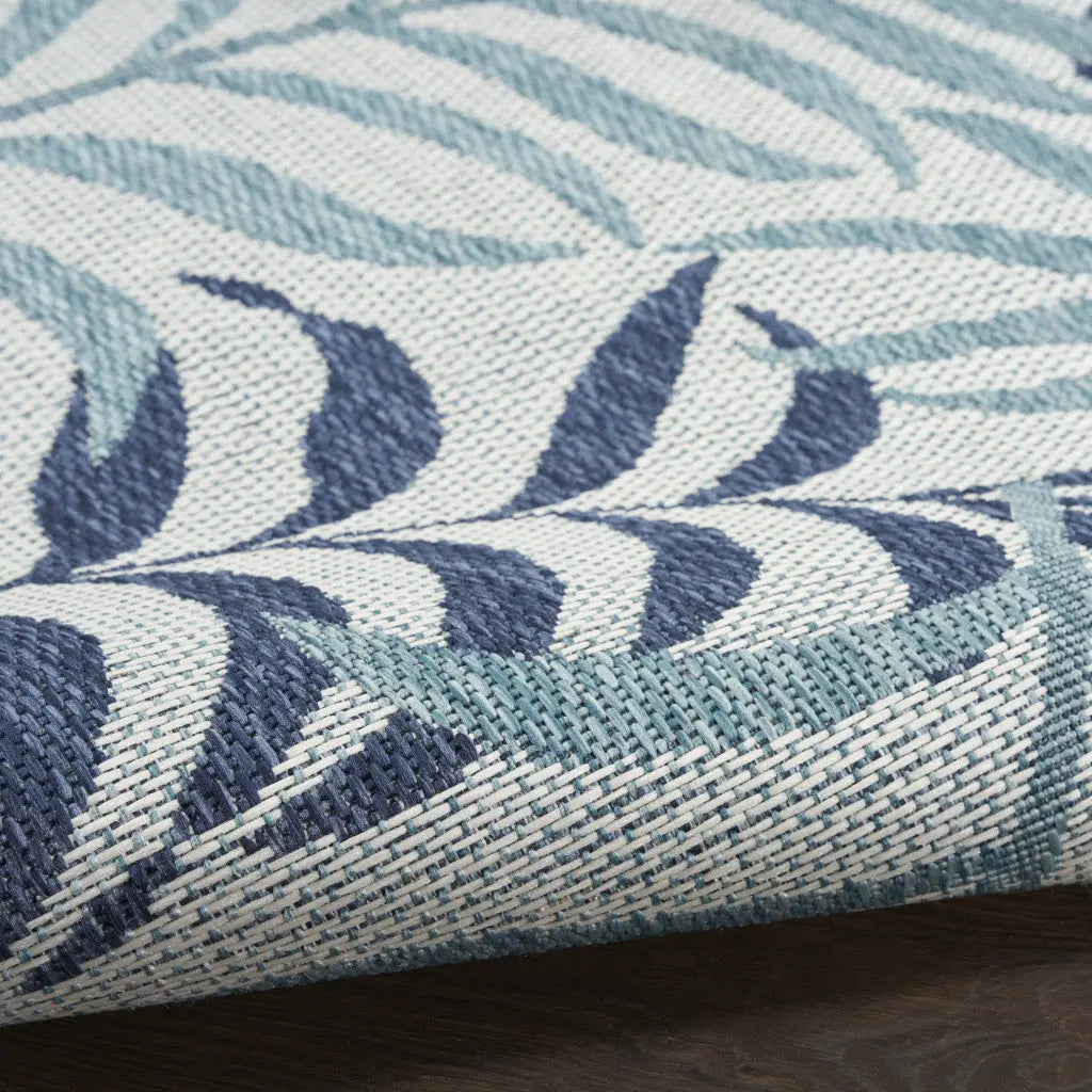 Blue and navy leaf-patterned woven rug on a textured cream background, perfect for modern and coastal decor.