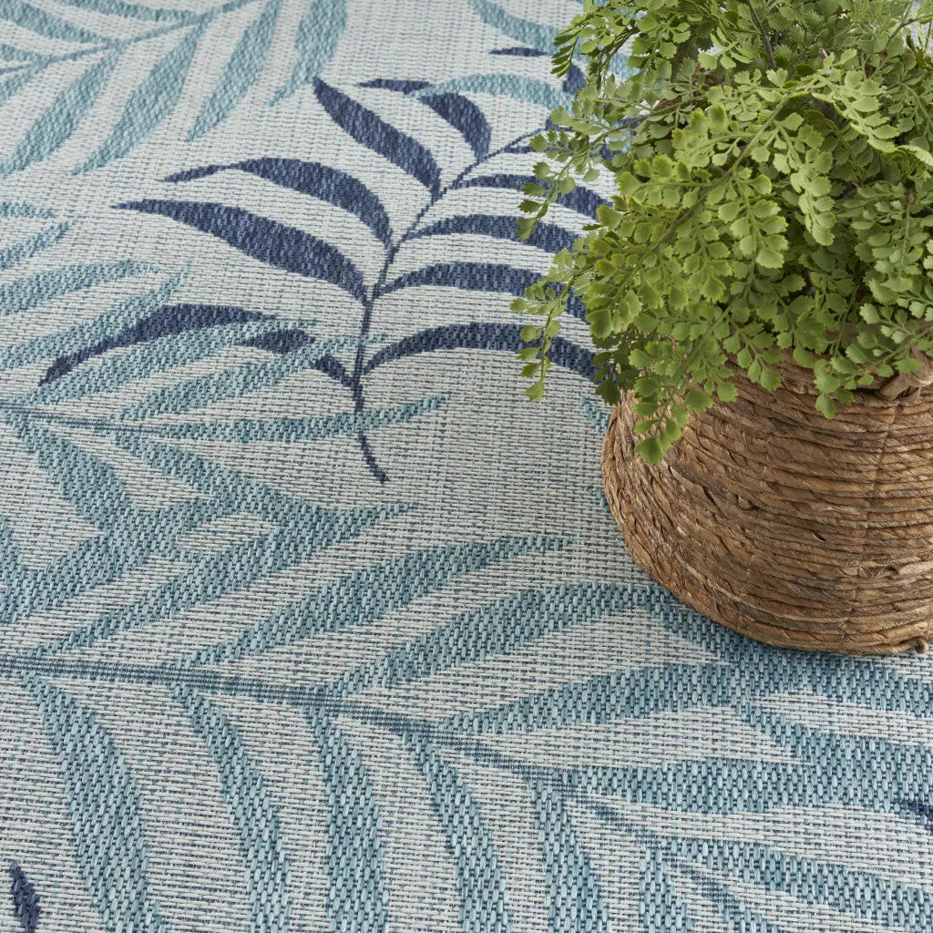 Blue and navy leaf-patterned indoor rug with a natural woven planter featuring greenery.