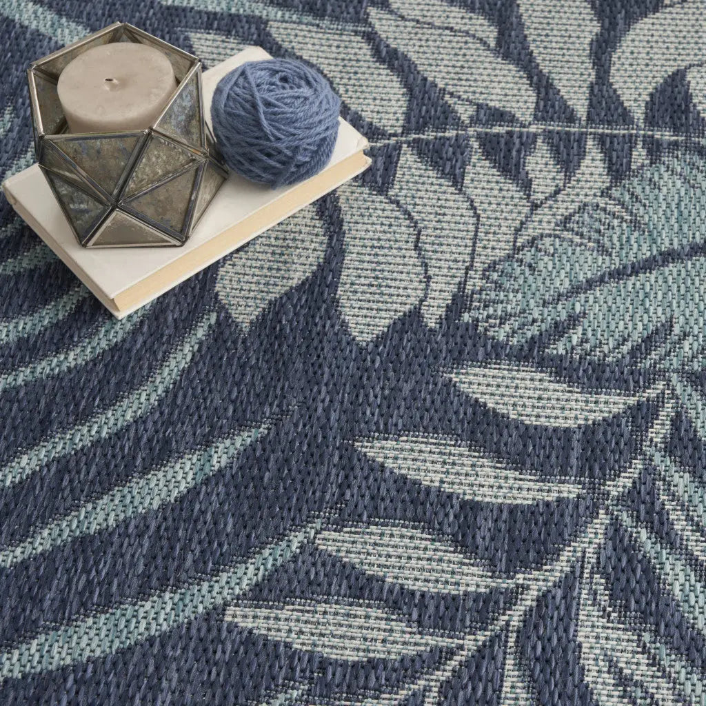 Navy blue leaf-patterned woven area rug with natural fibers, complemented by a geometric candle holder and yarn.