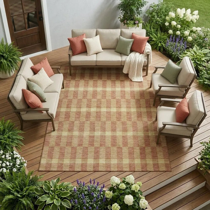 Beige outdoor seating set with coral and green cushions on a checkered rug, surrounded by lush greenery.