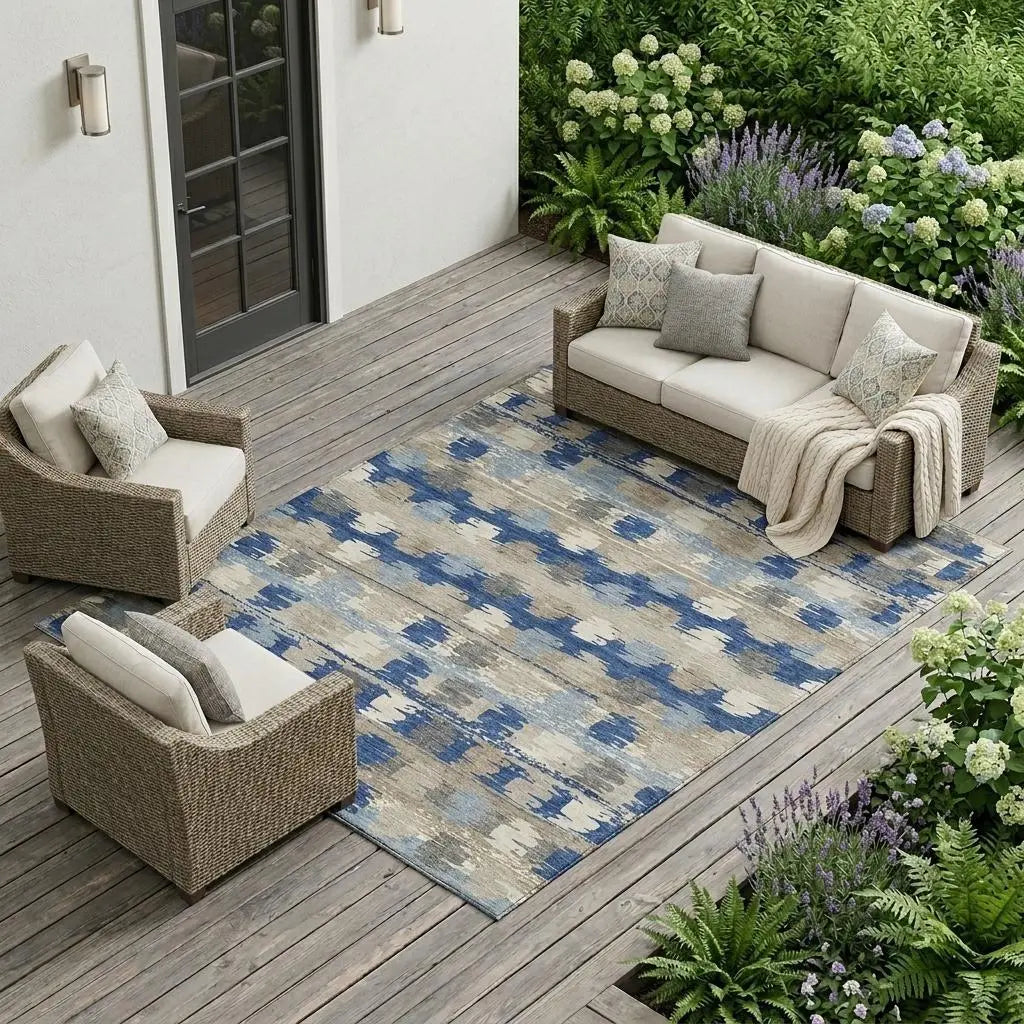 Blue and beige patterned outdoor rug on a wooden patio with wicker furniture and greenery.