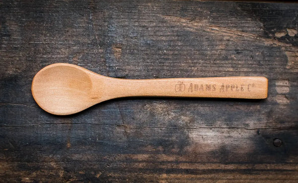 Handcrafted wooden spoon in natural finish with engraved "ADAMS APPLE CO." logo, perfect for kitchen use.