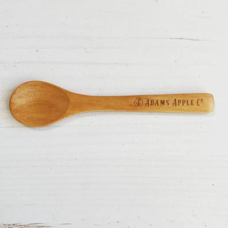 Natural wood spoon with engraved "ADAMS APPLE CO." logo, perfect for cooking and serving.
