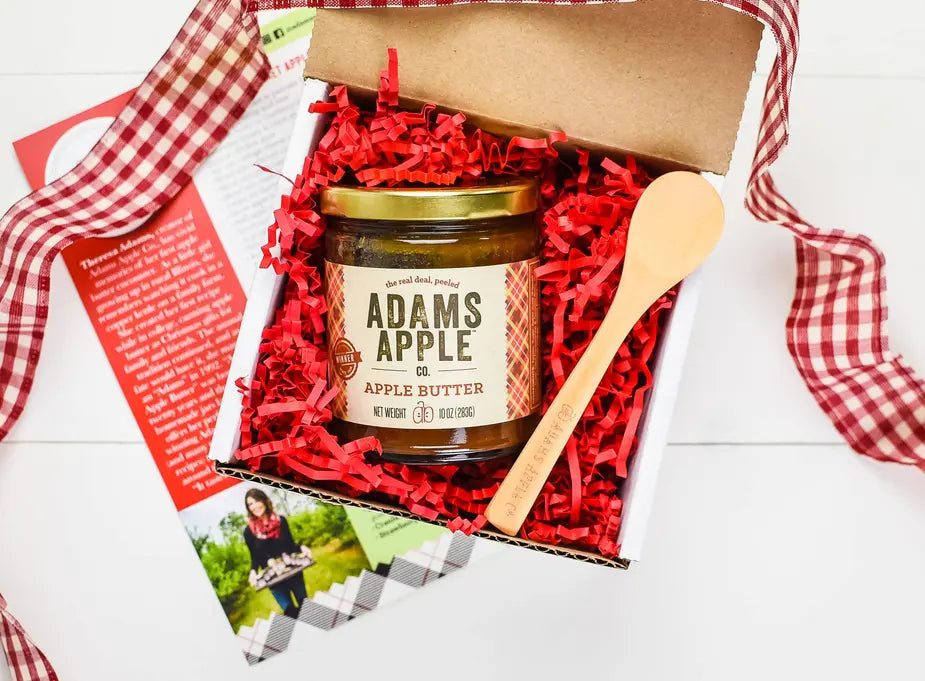 Adams Apple Co. apple butter in a glass jar with a wooden spoon, packaged in a rustic gift box with red crinkle paper.