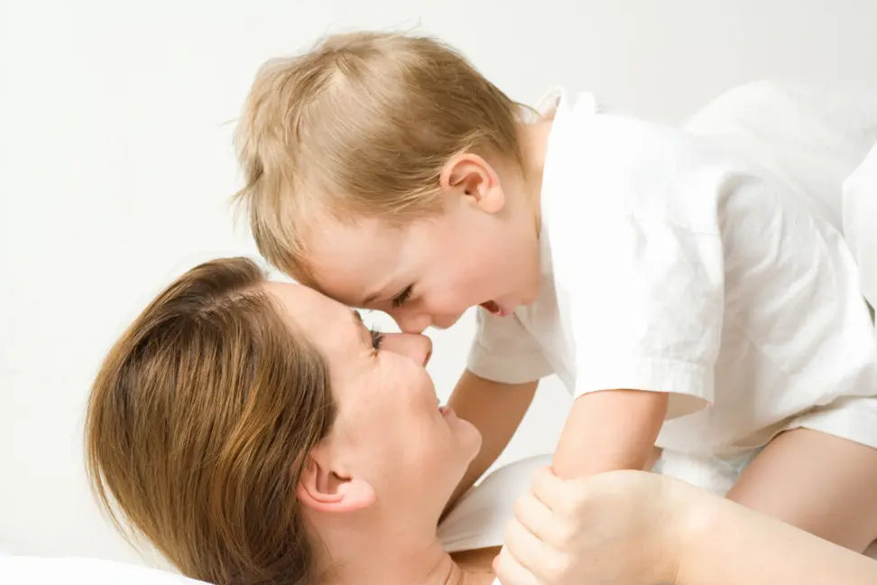 Mother and child smiling together, wearing white cotton shirts, capturing a joyful moment at home.