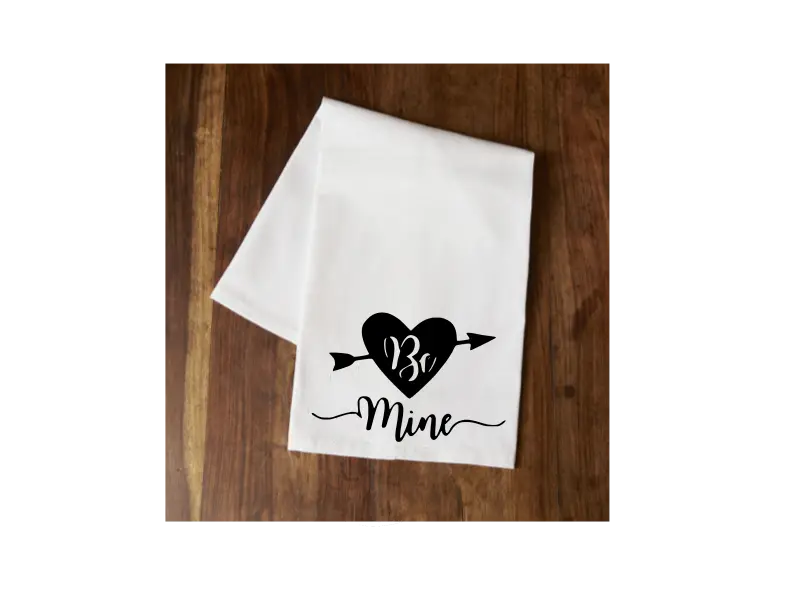 White cotton kitchen towel with black heart and arrow design, featuring the text "Be Mine" in a stylish font.