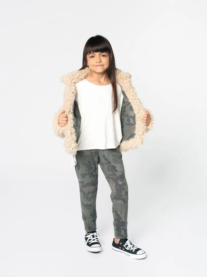 Girl's cozy beige faux fur coat, white top, and green camo pants, paired with black sneakers. Perfect for stylish comfort.